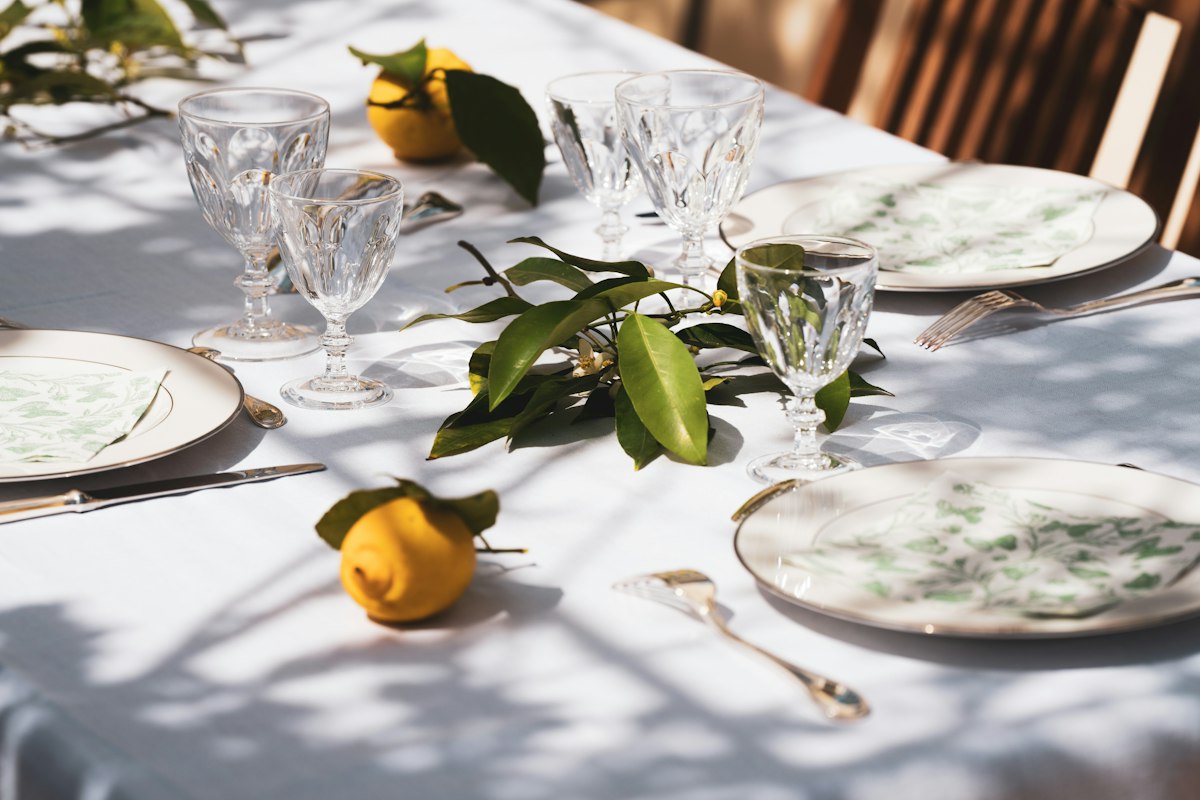 Sunlit dining table set with plates, crystal glasses, and lemons