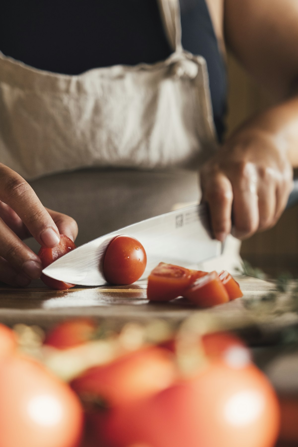 Hands slicing a tomato with a chef's knife on a wooden board